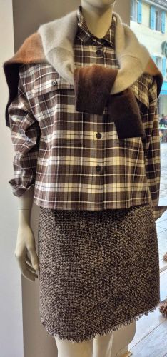Ensemble féminin automnal avec chemise à carreaux marron, jupe en tweed et pull noué sur les épaules.
