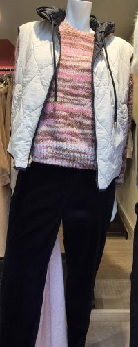Doudoune sans manches blanche avec capuche noire, associée à un pull rose chiné et un pantalon noir.
