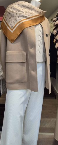 enue féminine chic avec veste beige, pull blanc torsadé, pantalon blanc et foulard imprimé.
